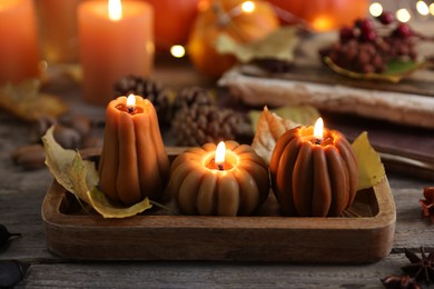 Photo of Burning candles in shape of pumpkins and autumn decor on wooden table