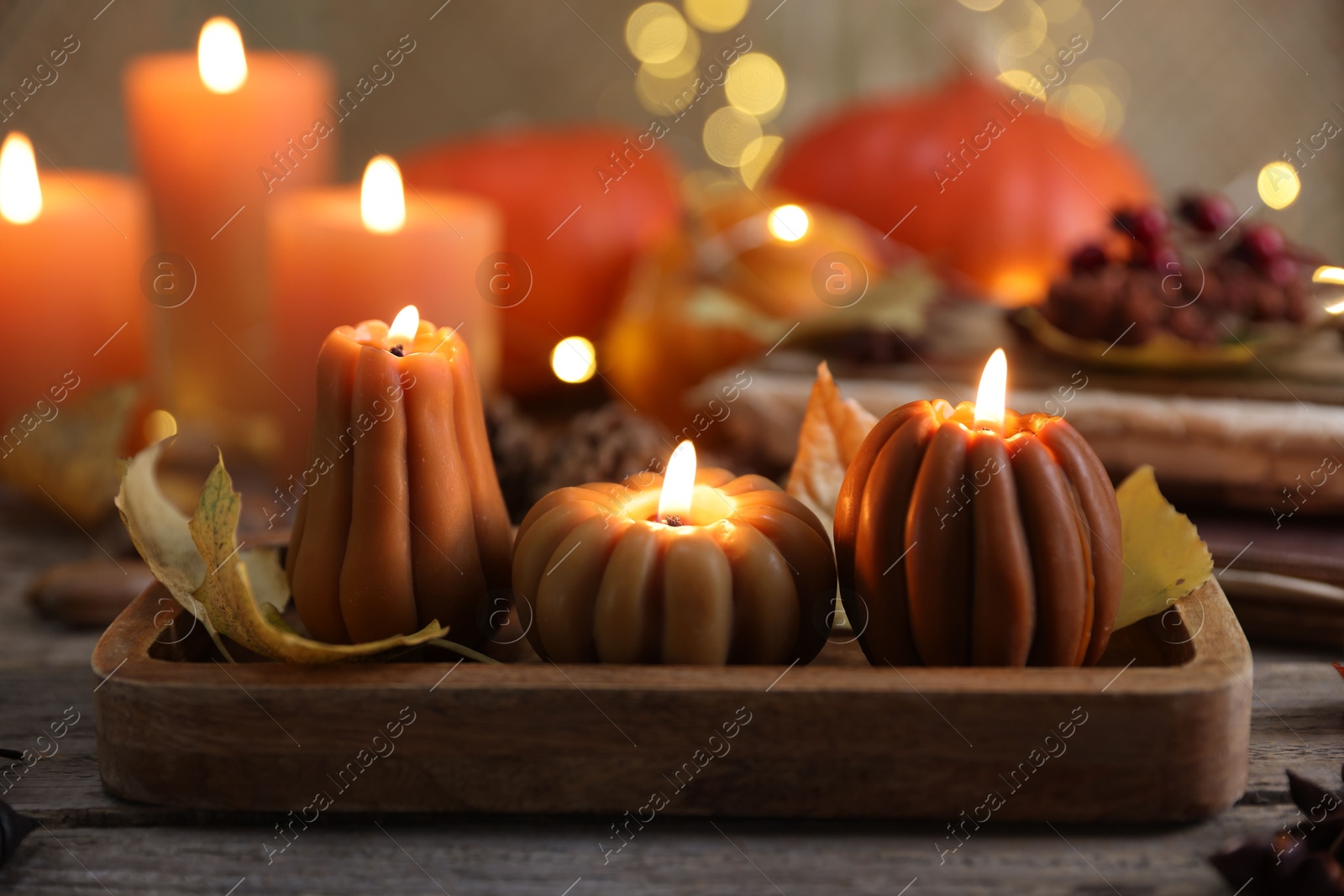 Photo of Burning candles in shape of pumpkins and autumn decor on wooden table