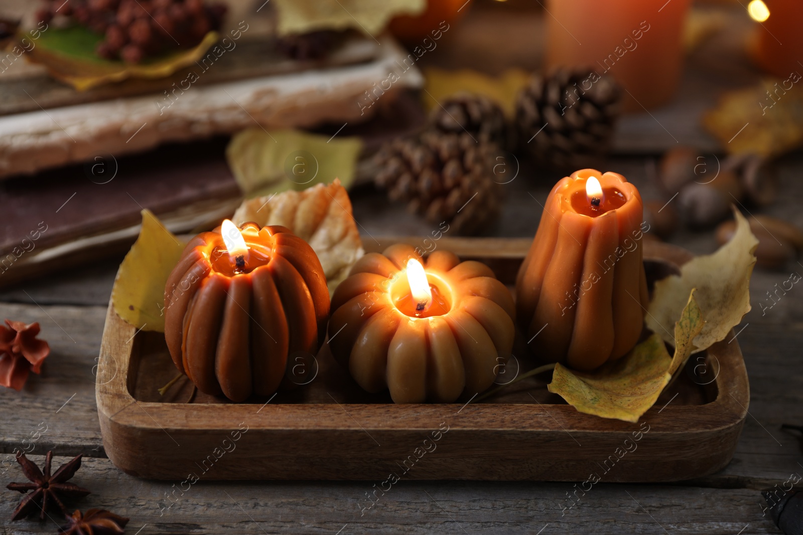 Photo of Burning candles in shape of pumpkins and autumn decor on wooden table