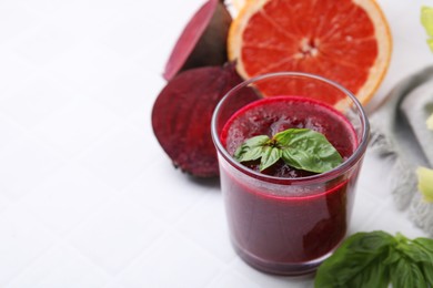 Photo of Vegan drink. Tasty beetroot smoothie in glass, fresh vegetables, grapefruit and basil on white tiled table, closeup. Space for text