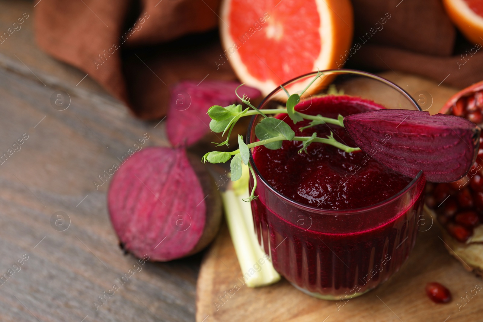 Photo of Tasty beetroot smoothie with microgreens in glass, fresh vegetables and fruits on wooden table, closeup. Vegan drink