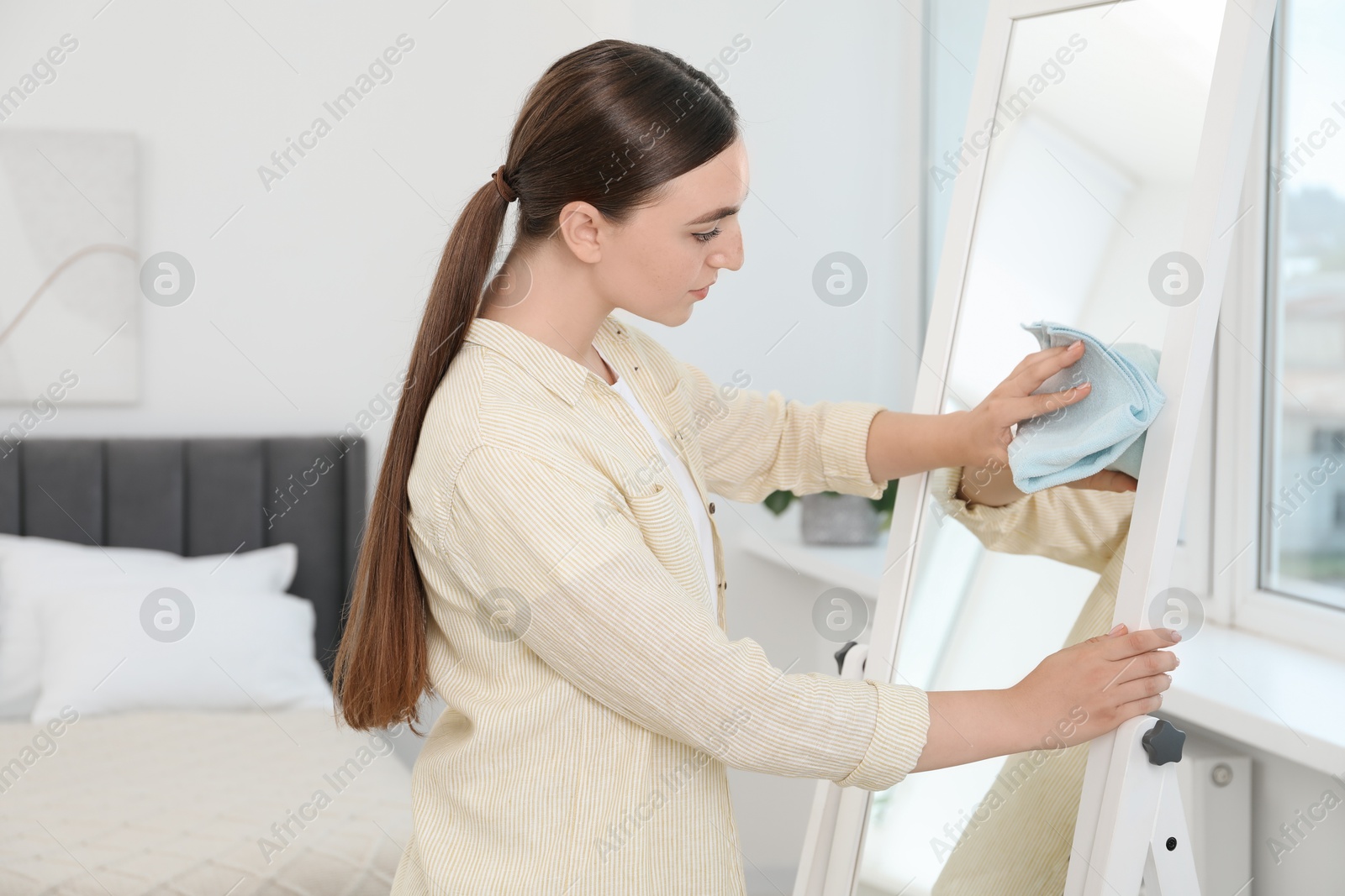 Photo of Beautiful young woman cleaning mirror with rag at home