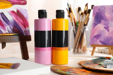 Photo of Acrylic paints of different colors, small easels, palettes and brushes on light table indoors