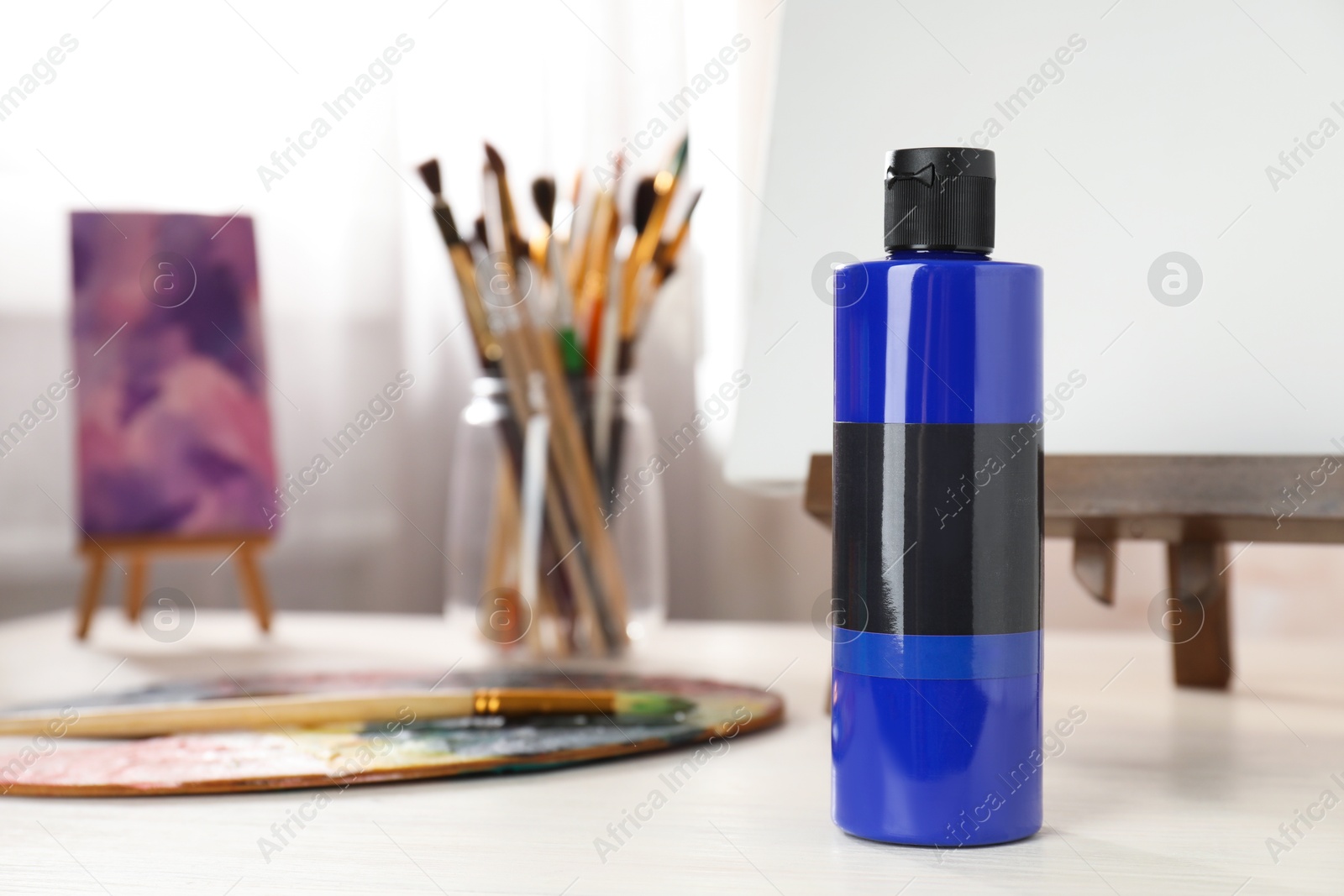 Photo of Blue acrylic paint in bottle, small easels, palette and brushes on wooden table indoors