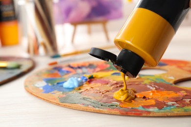 Squeezing red acrylic paint on palette at wooden table indoors, closeup