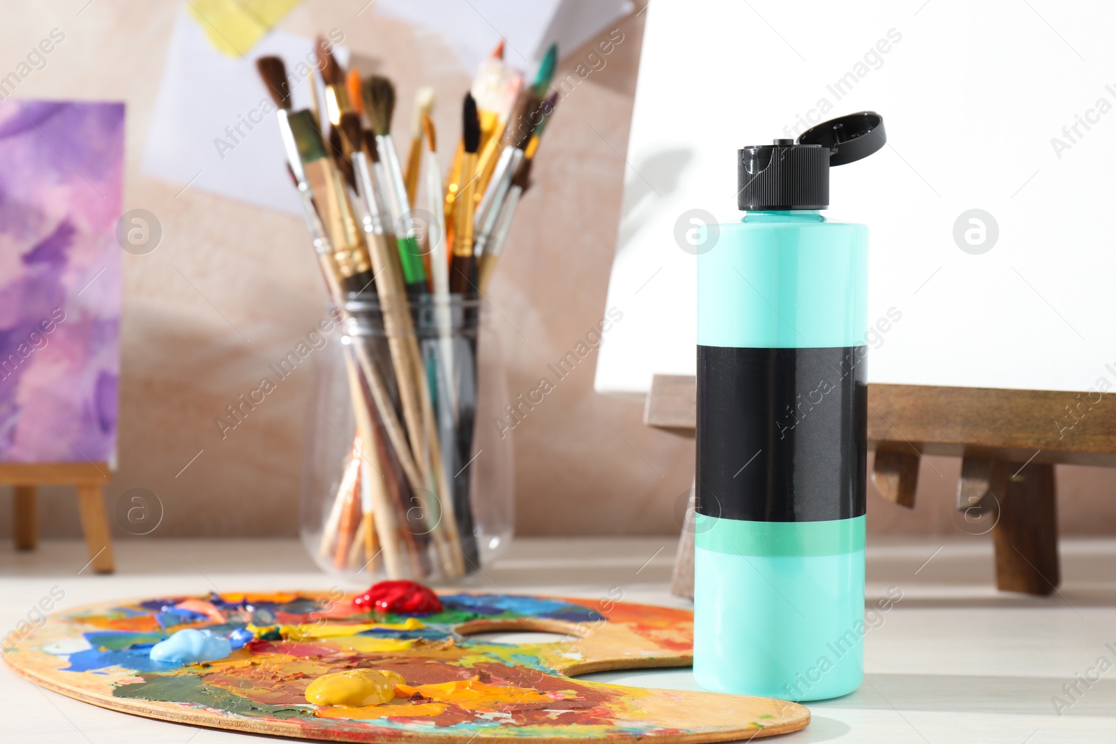 Photo of Turquoise acrylic paint in bottle, small easels, palette and brushes on wooden table indoors