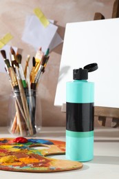 Photo of Turquoise acrylic paint in bottle, small easel, palette and brushes on wooden table indoors