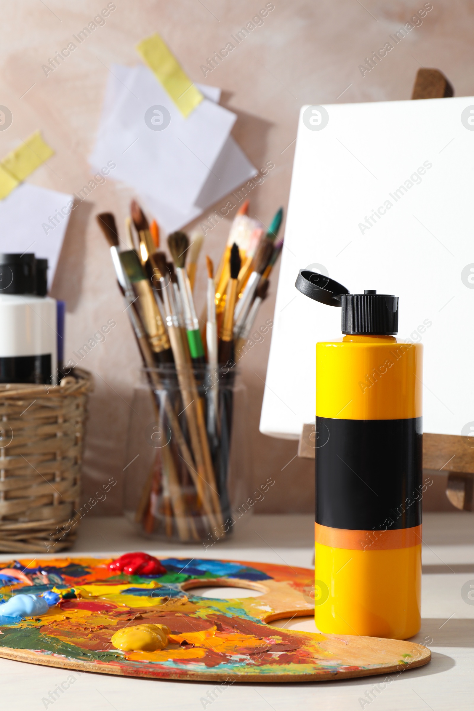 Photo of Orange acrylic paint in bottle, small easel, palette and brushes on wooden table indoors