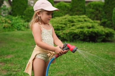 Photo of Little girl watering lawn with hose in backyard