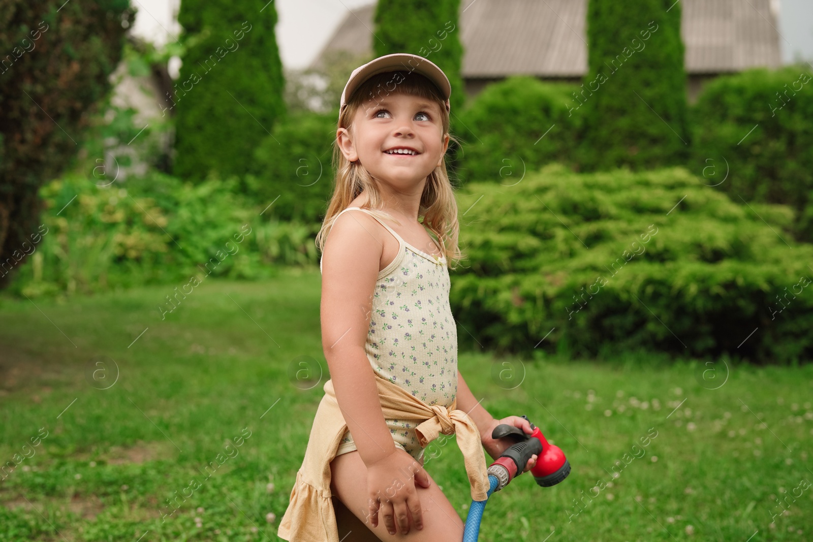 Photo of Little girl watering lawn with hose in backyard