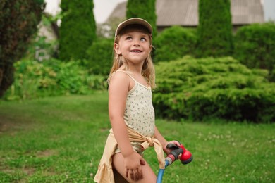 Photo of Little girl watering lawn with hose in backyard