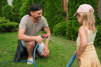 Photo of Father and his daughter watering lawn with hose in backyard, selective focus