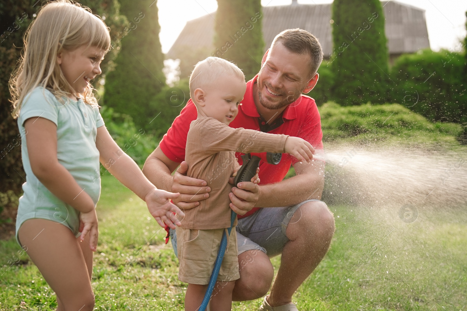 Photo of Little boy watering lawn with hose while his father and sister watching in backyard