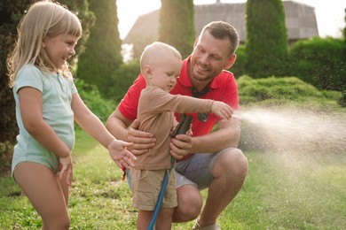 Little boy watering lawn with hose while his father and sister watching in backyard