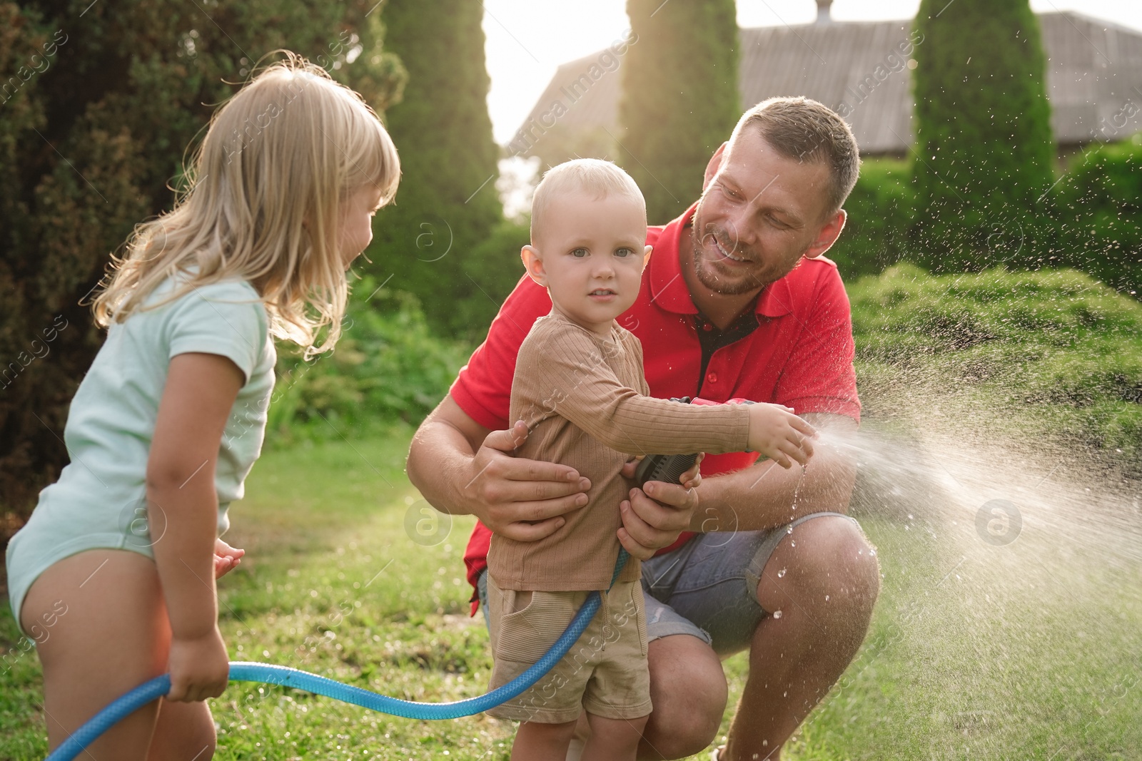 Photo of Little boy watering lawn with hose while his father and sister watching in backyard