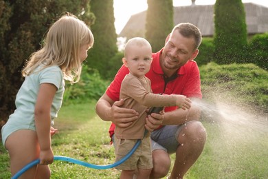 Little boy watering lawn with hose while his father and sister watching in backyard