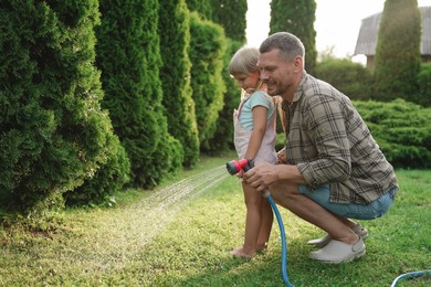 Little girl and her father watering lawn with hose in backyard