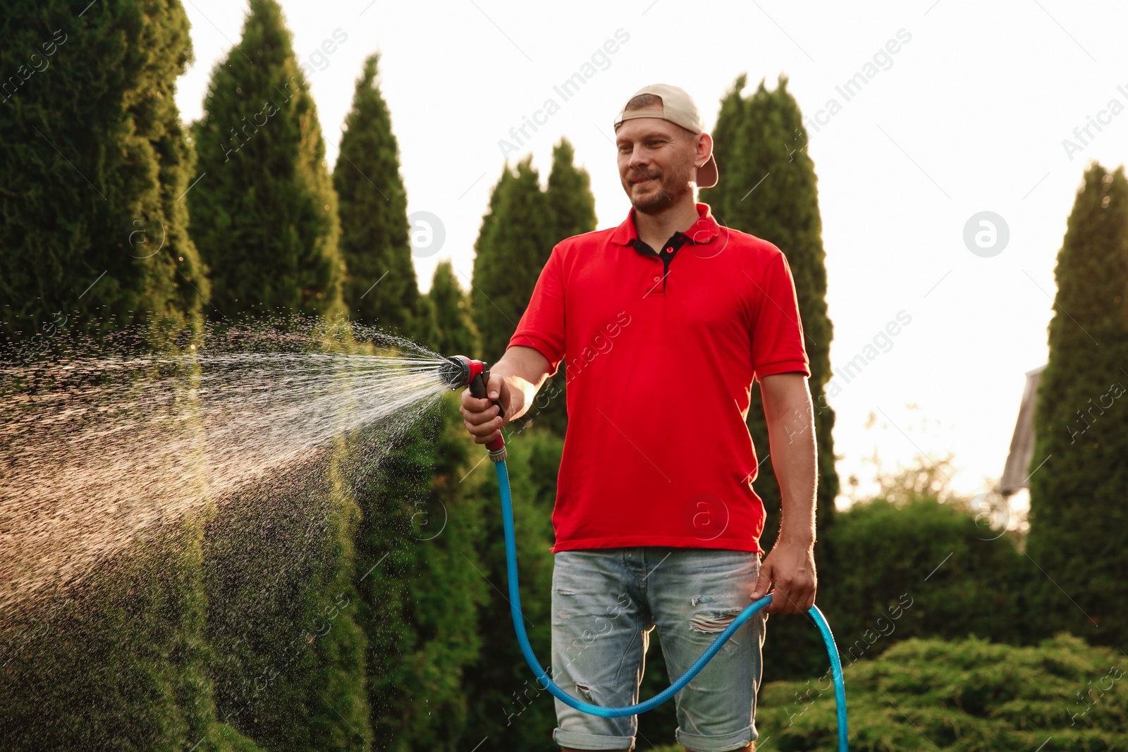 Photo of Man watering lawn with hose in backyard