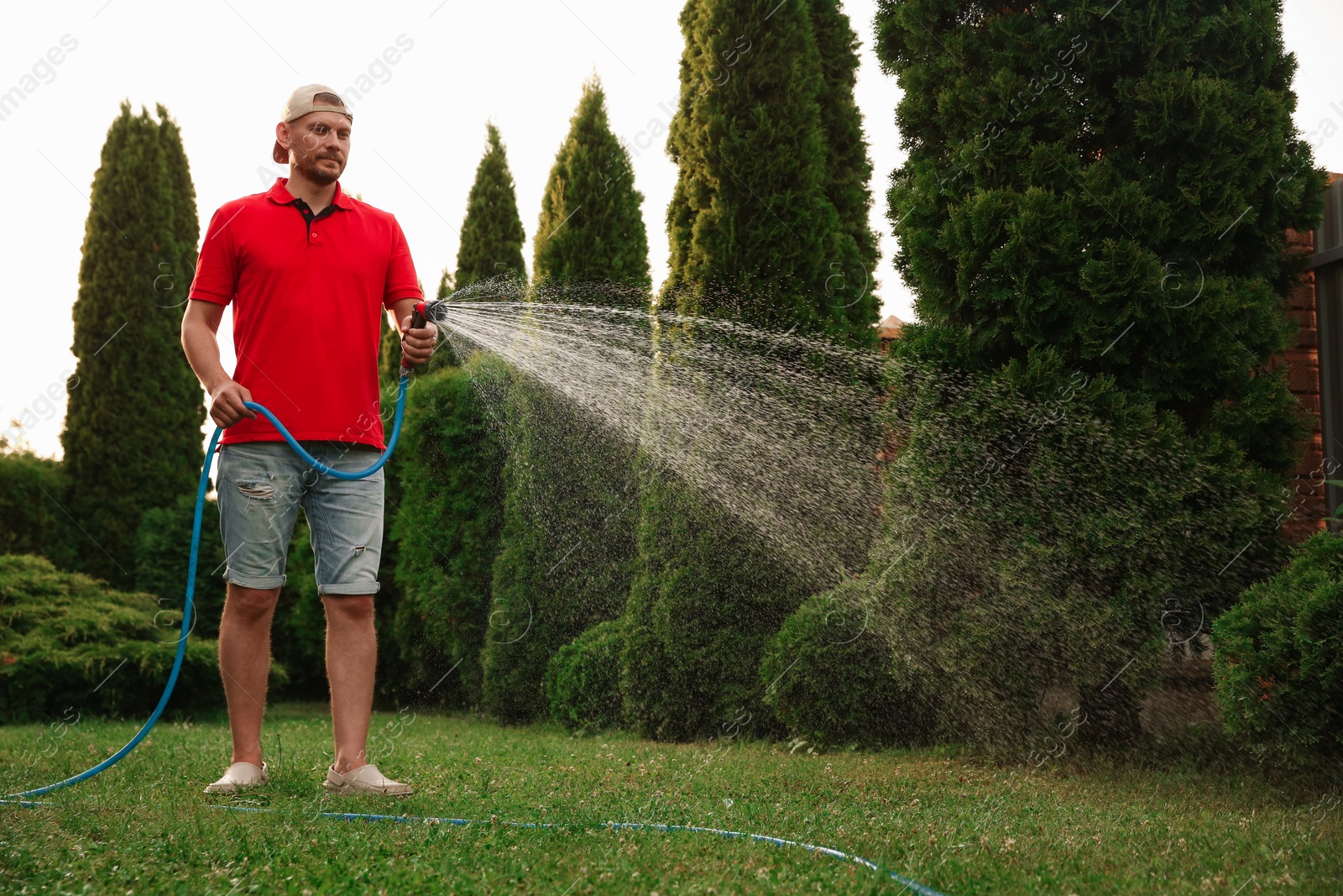 Photo of Man watering lawn with hose in backyard