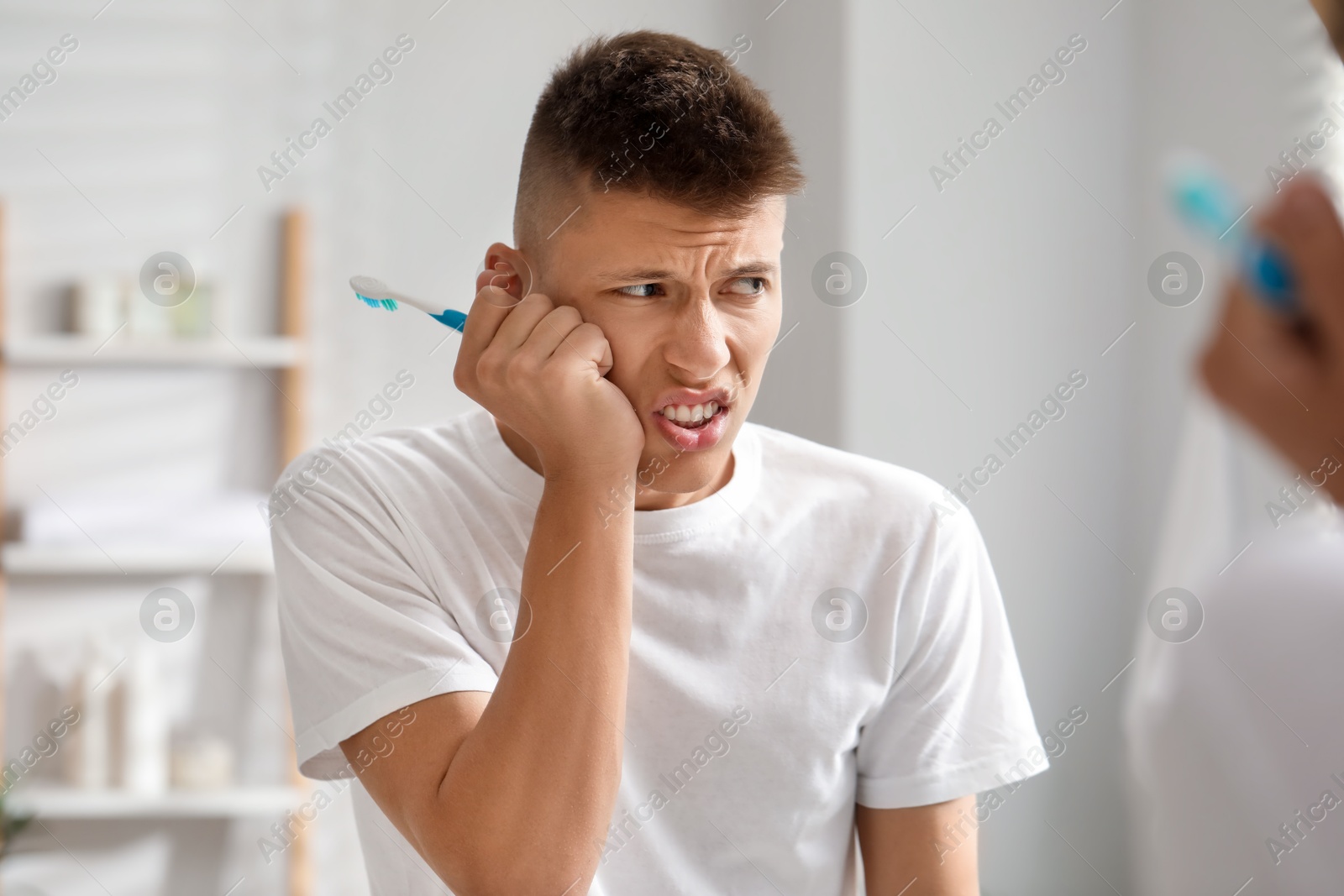 Photo of Young man with toothbrush suffering from toothache in bathroom