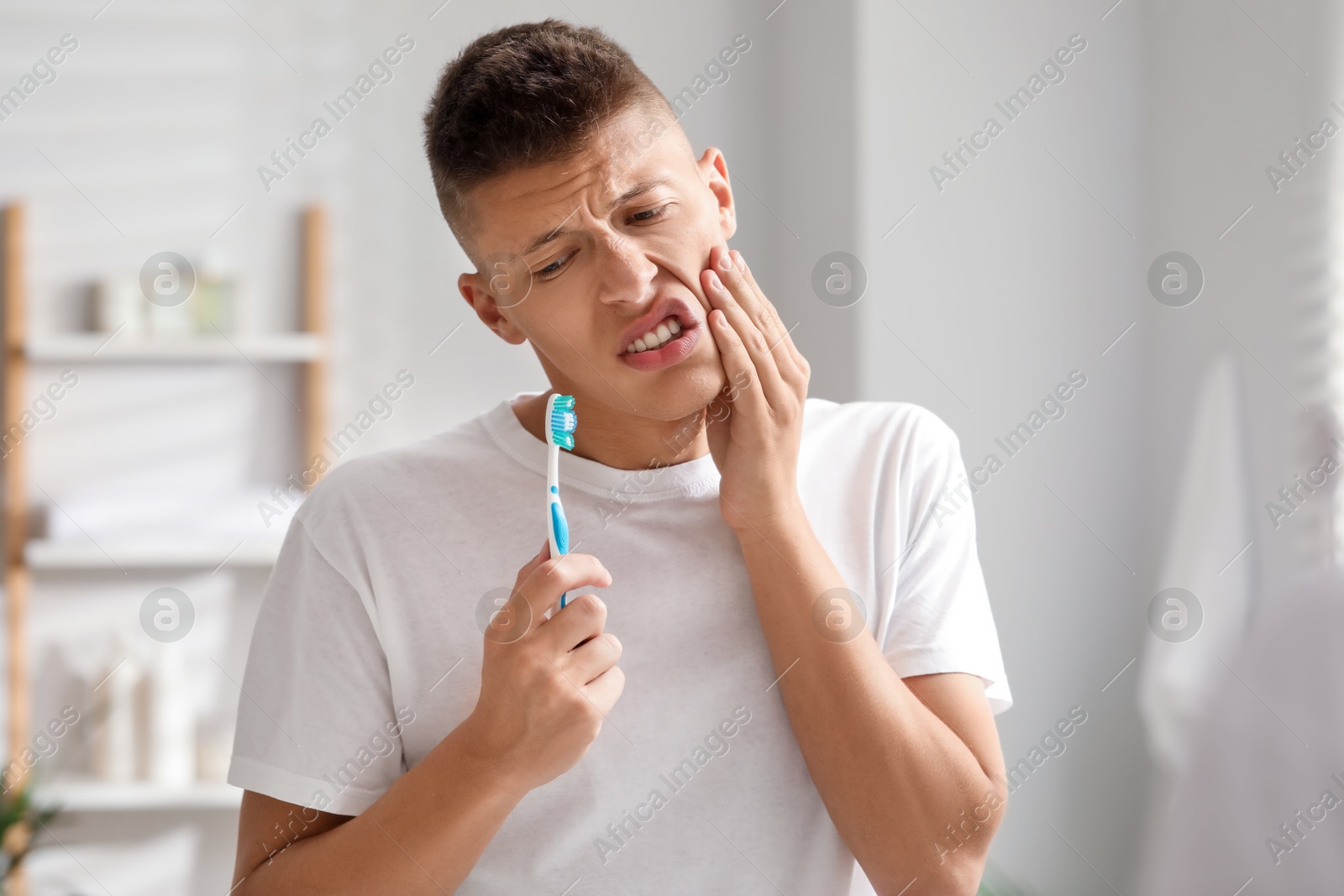 Photo of Young man with toothbrush suffering from toothache in bathroom