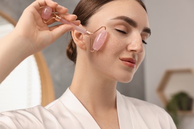 Photo of Beautiful young woman doing facial massage with roller at home