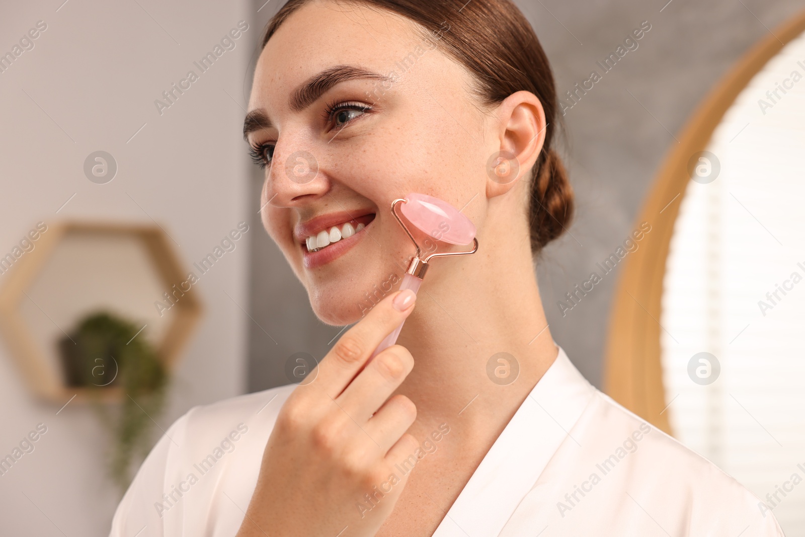 Photo of Beautiful young woman doing facial massage with roller at home