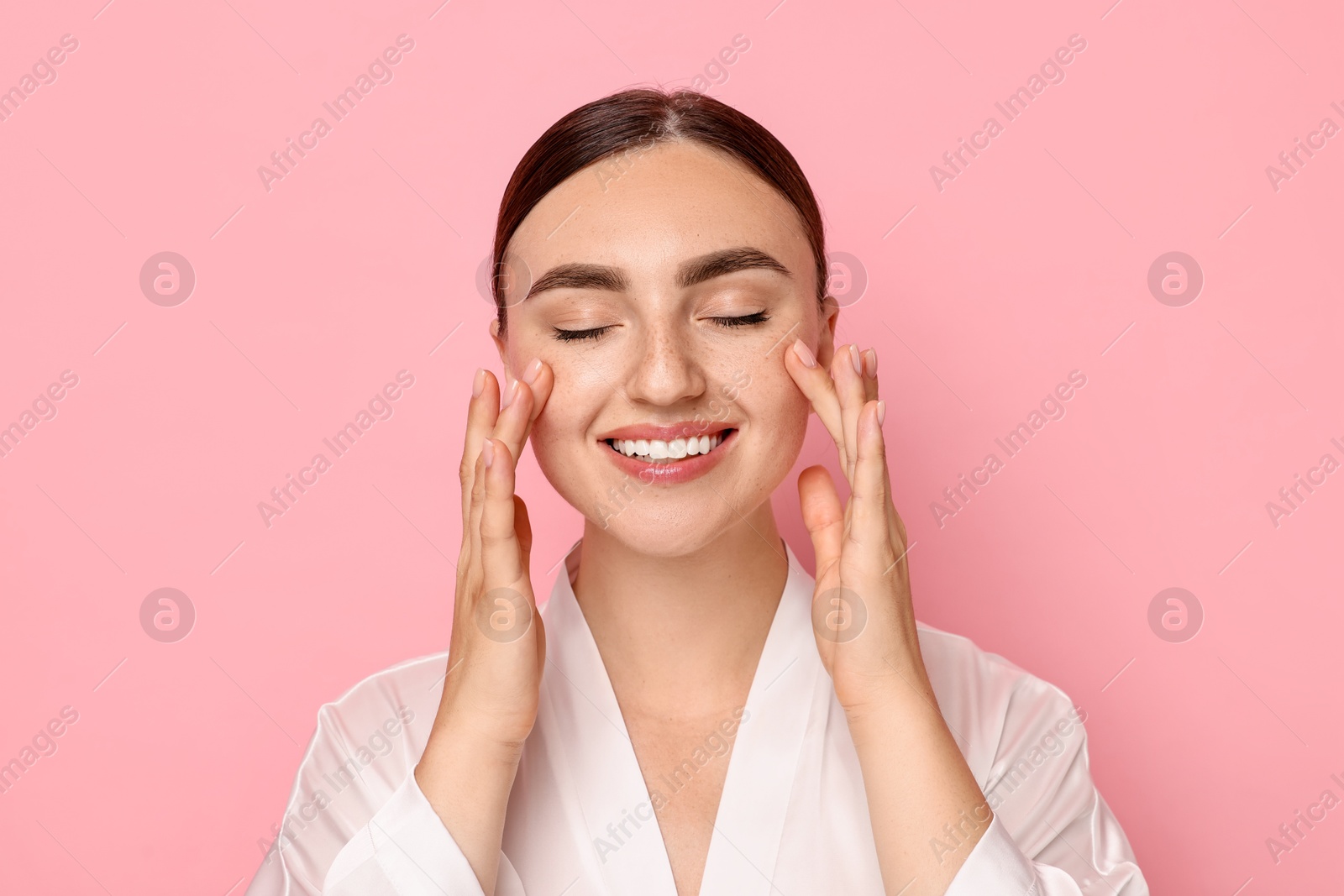 Photo of Beautiful young woman doing facial massage on pink background