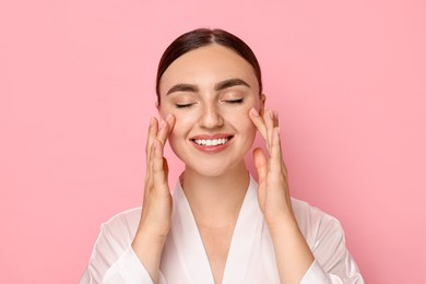 Beautiful young woman doing facial massage on pink background