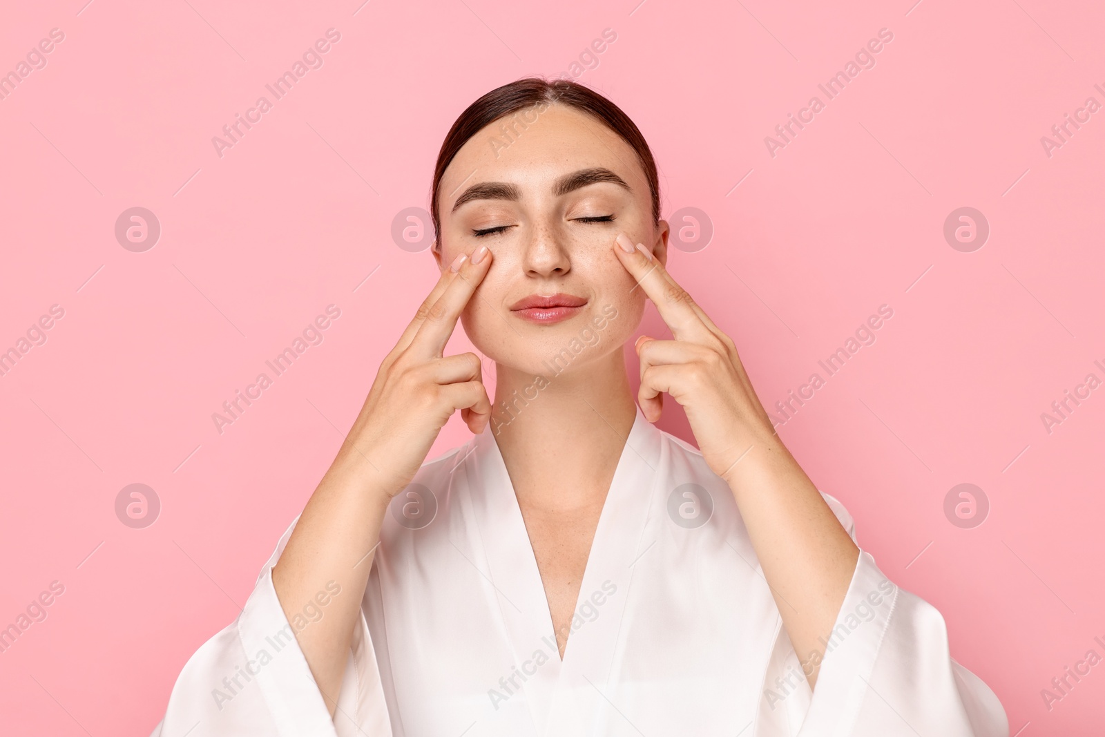 Photo of Beautiful young woman doing facial massage on pink background