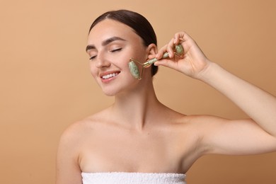 Beautiful young woman doing facial massage with roller on beige background