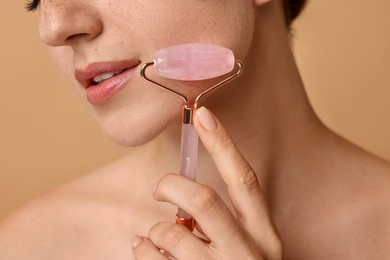 Photo of Woman doing facial massage with roller on beige background, closeup