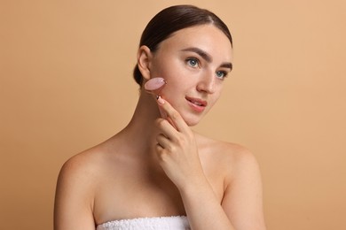 Beautiful young woman doing facial massage with roller on beige background