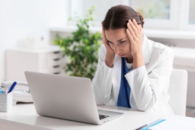 Photo of Tired nurse at white table with laptop in clinic