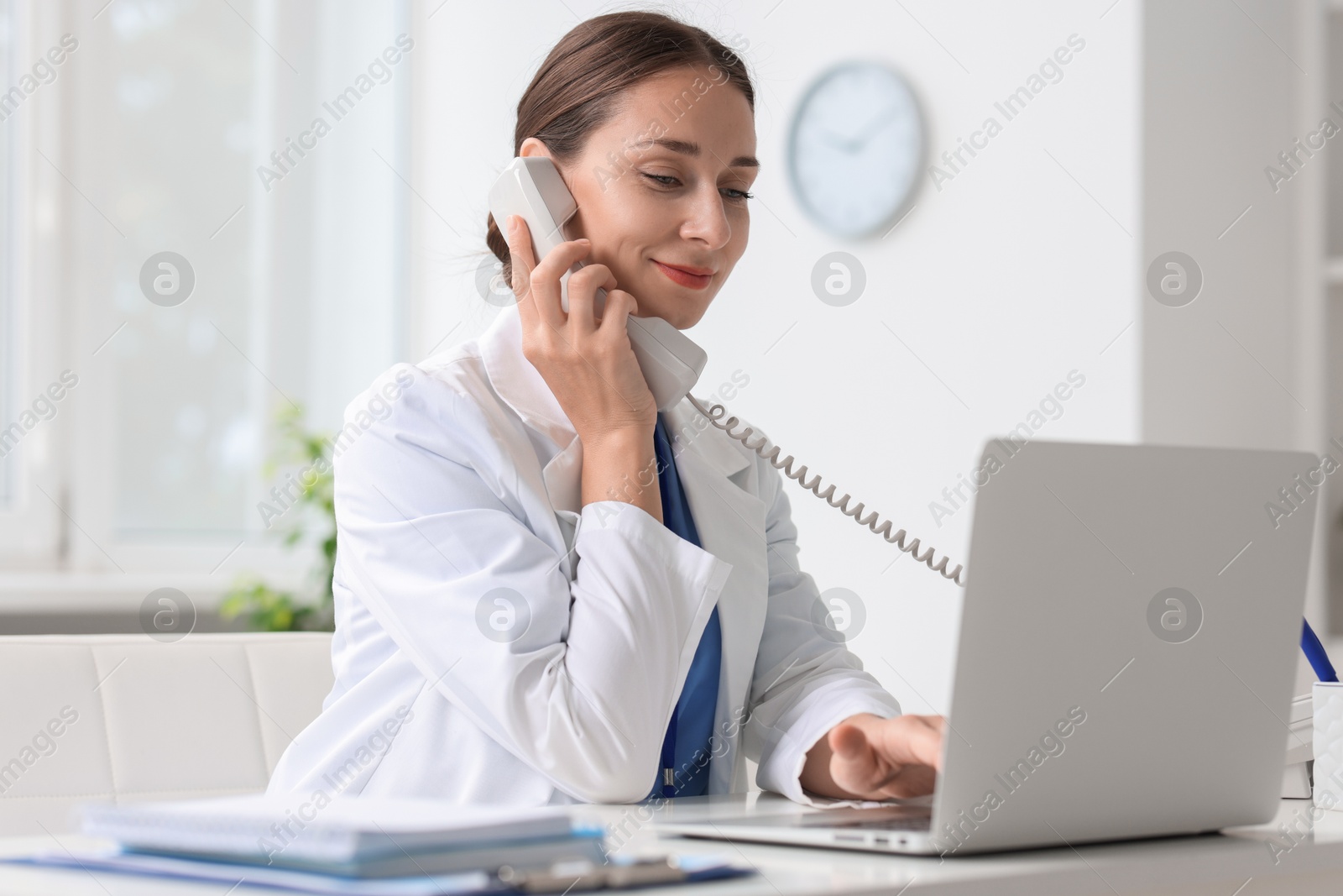 Photo of Nurse consulting patient by phone at table in clinic