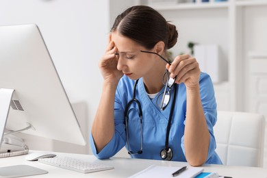 Tired nurse with glasses at white table in clinic