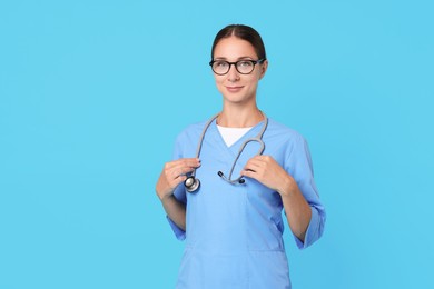 Photo of Nurse in medical uniform with stethoscope on light blue background