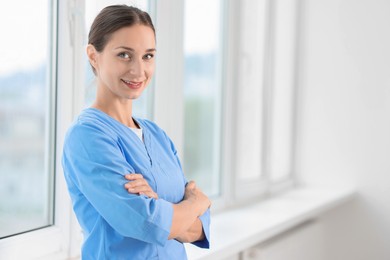 Nurse in medical uniform near window indoors, space for text