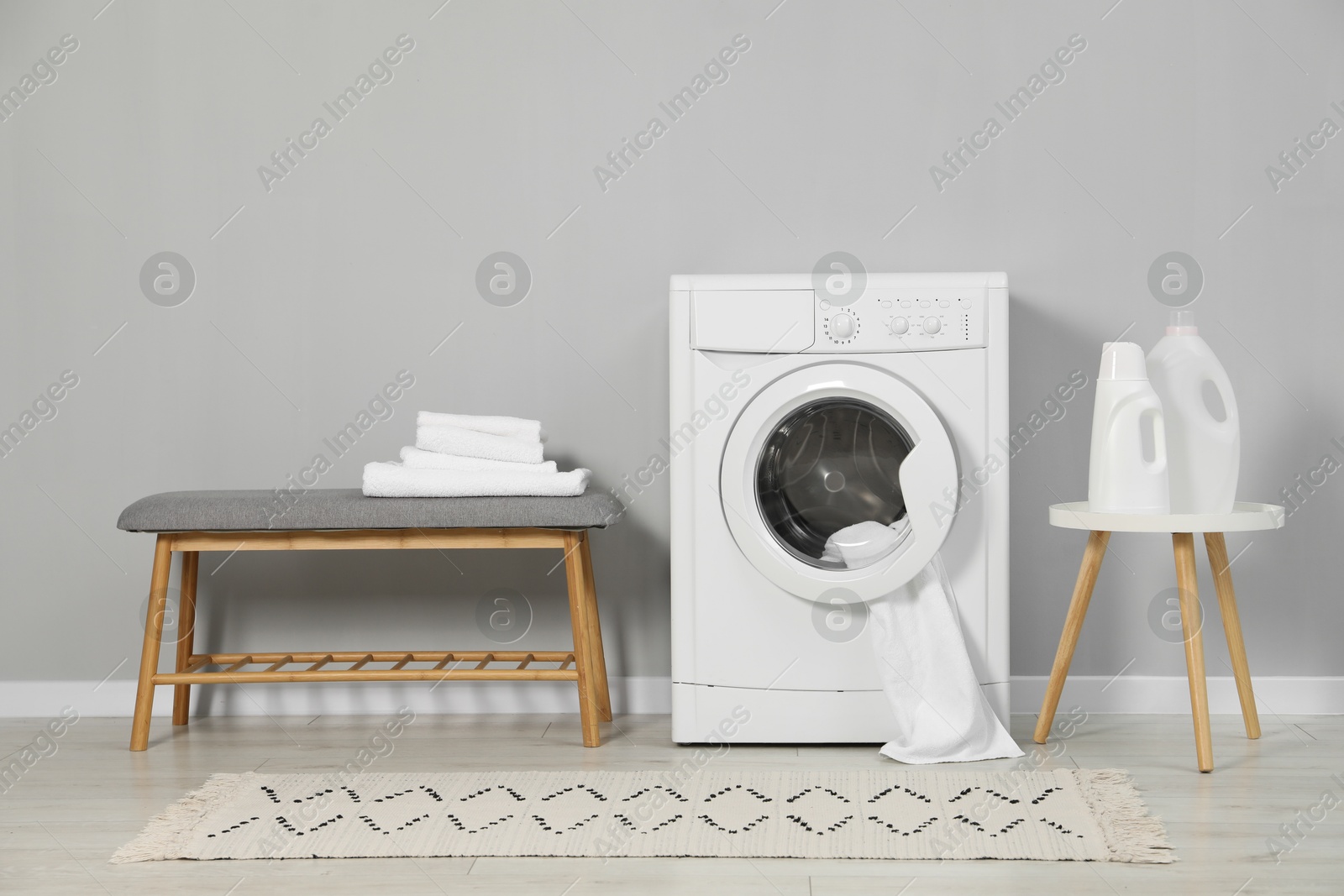 Photo of Washing machine, towels and detergents near grey wall