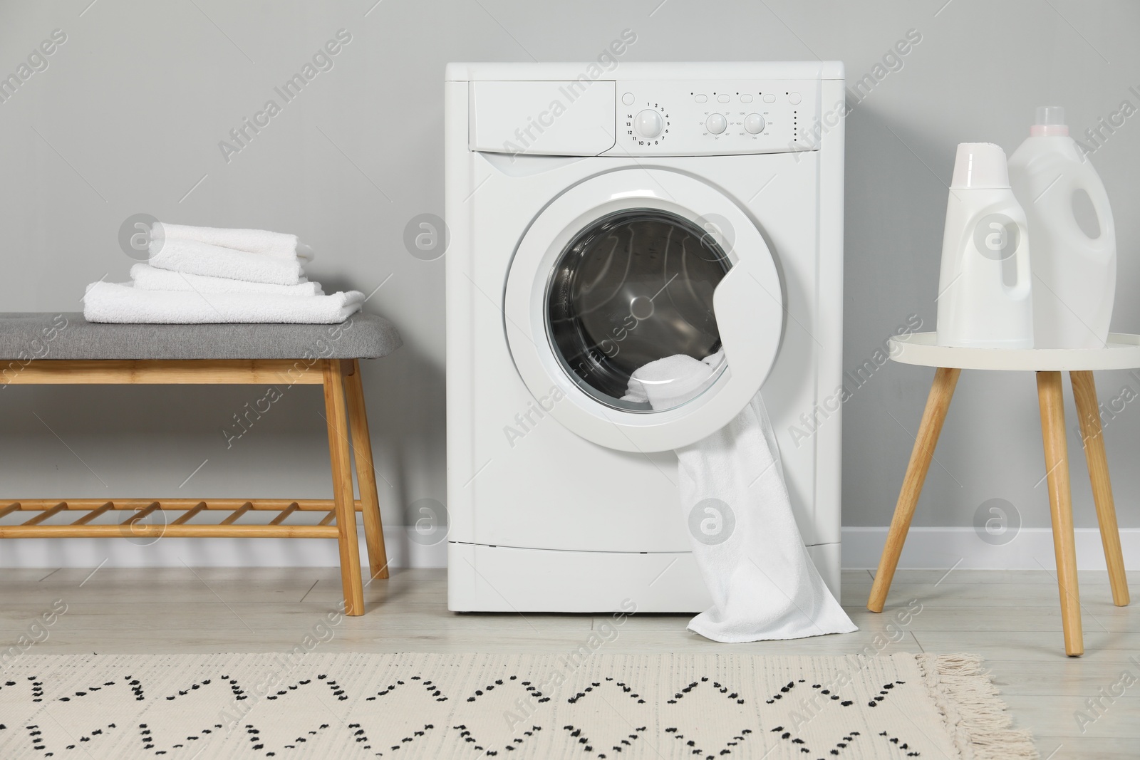 Photo of Washing machine, towels and detergents near grey wall