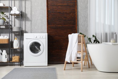 Photo of Washing machine, towels and detergents in bathroom