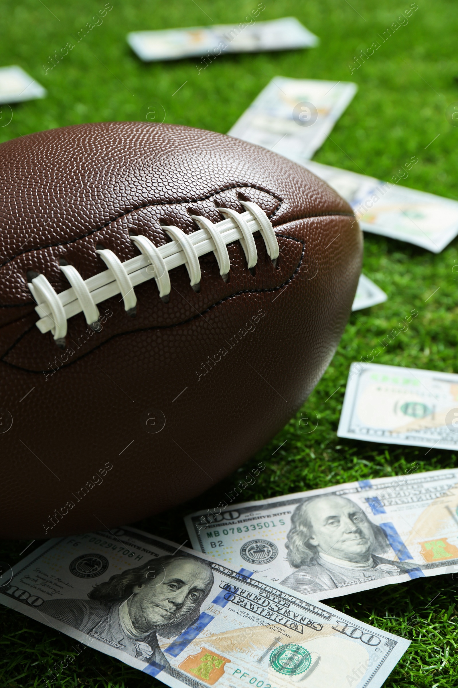 Photo of American football ball and dollar banknotes on green grass outdoors, closeup