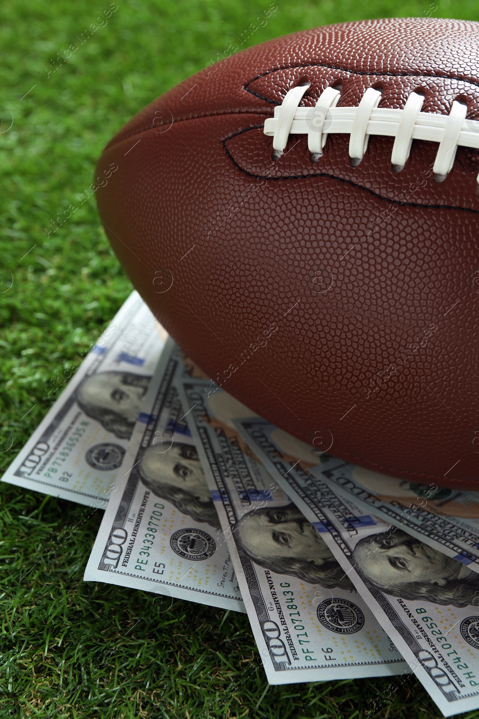 Photo of American football ball and dollar banknotes on green grass outdoors, closeup