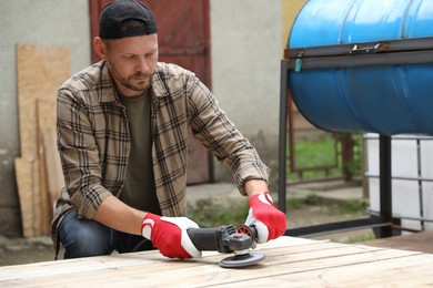 Man polishing wooden planks with angle grinder outdoors