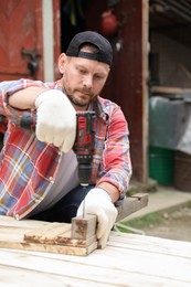 Man twisting screw into wooden plank with electric screwdriver outdoors