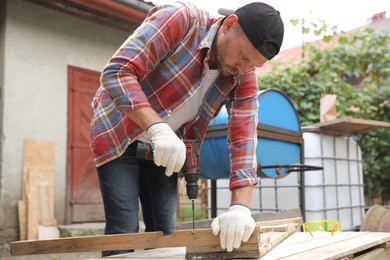 Man twisting screw into wooden plank with electric screwdriver outdoors