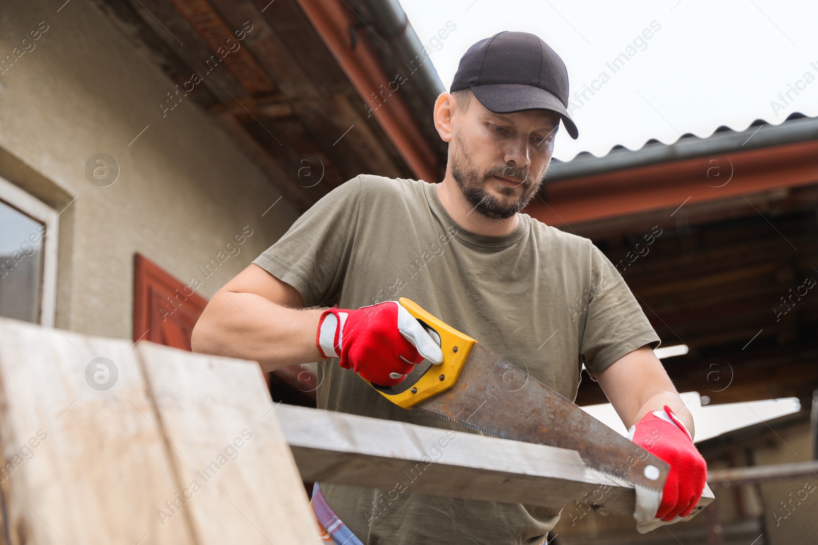 Photo of Handsome man sawing wooden plank in backyard