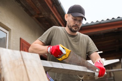 Handsome man sawing wooden plank in backyard