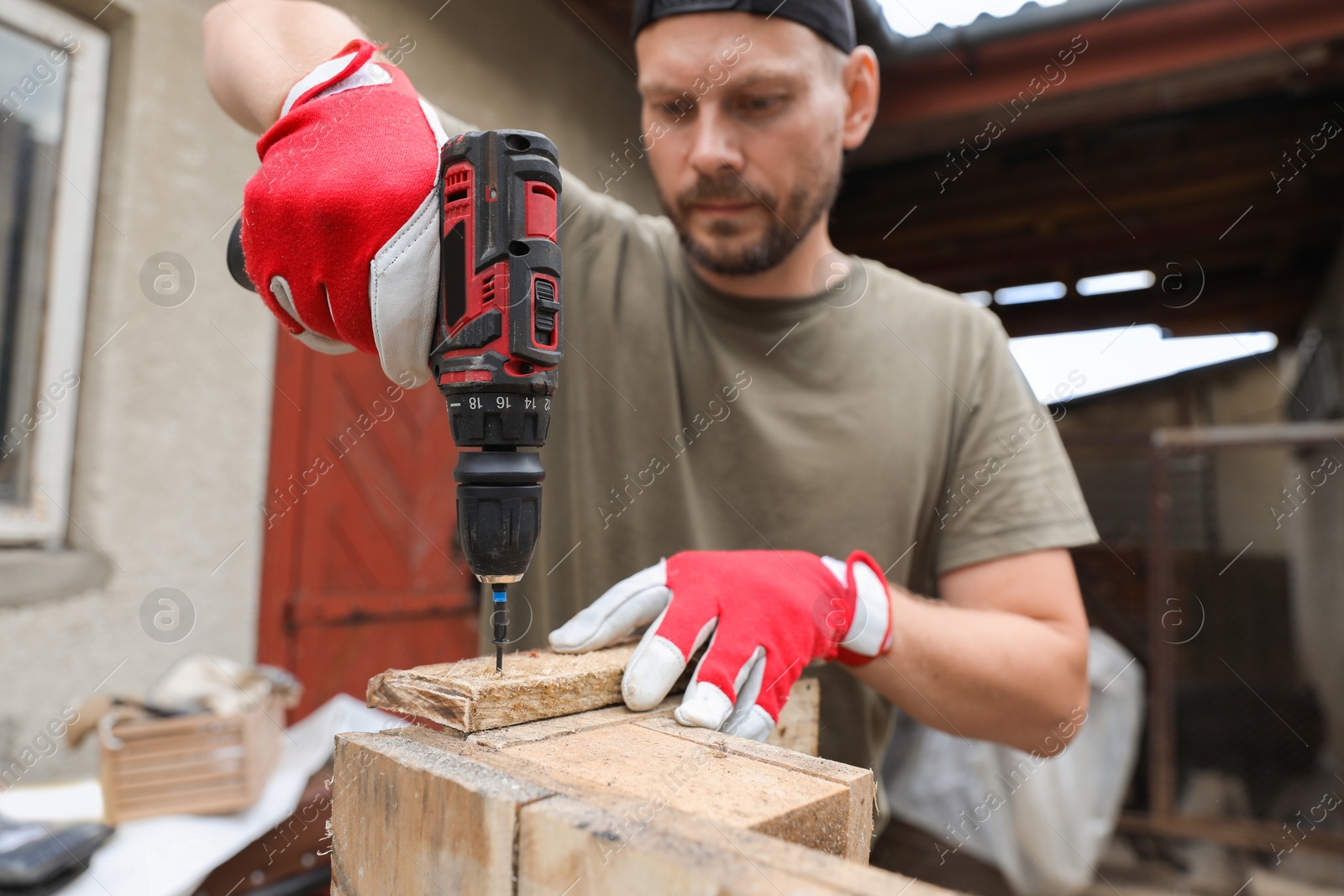 Photo of Man twisting screw into wooden plank with electric screwdriver outdoors, selective focus