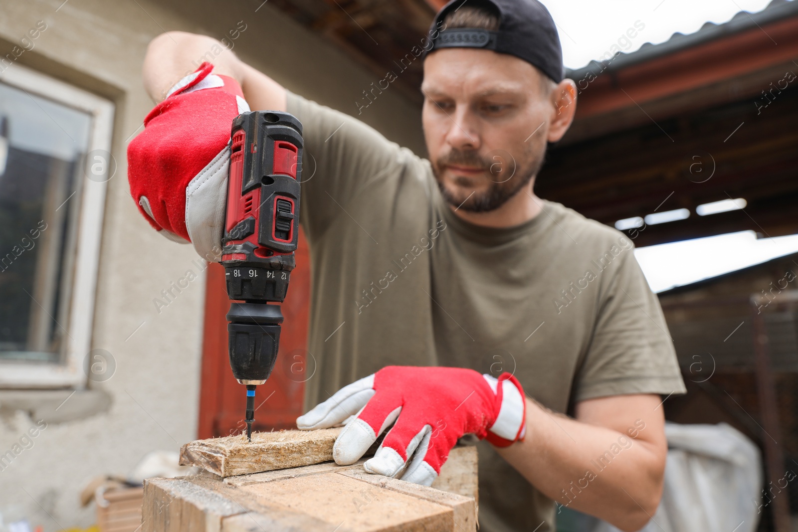 Photo of Man twisting screw into wooden plank with electric screwdriver outdoors, selective focus